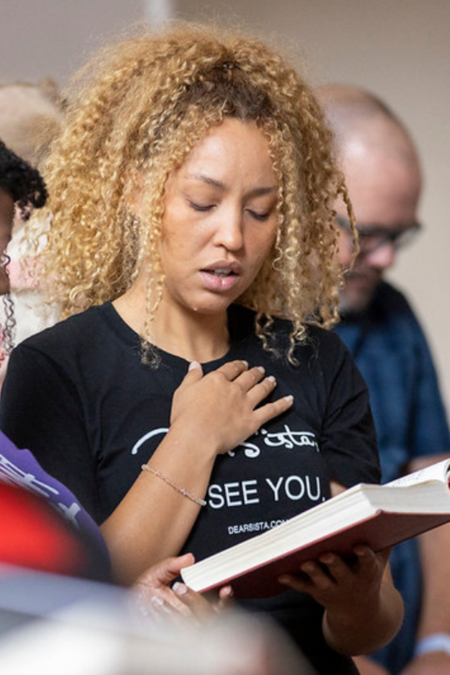 Person in a worship service reading a book with their hand on their chest.